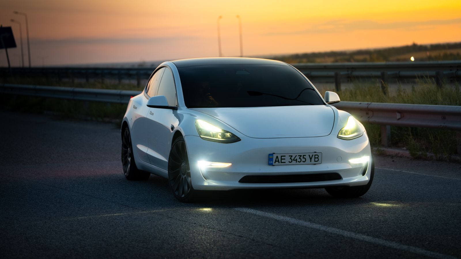 Sleek white electric car driving on a highway during a stunning sunset in Dnipro, Ukraine.