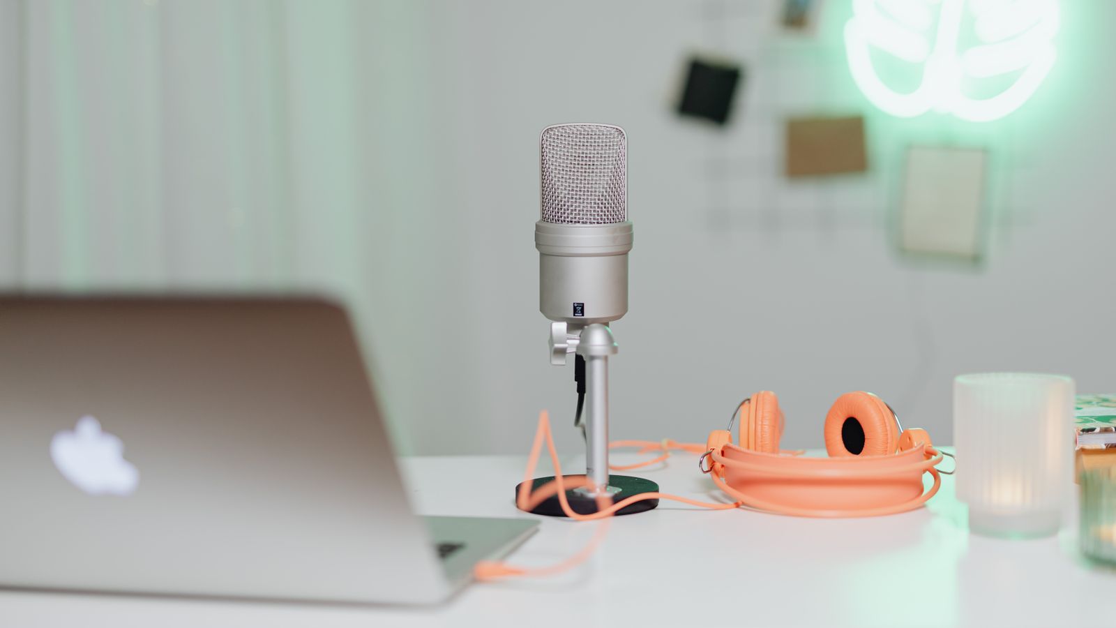 A modern desk setup featuring a condenser microphone, laptop, and headphones in a stylish workspace.