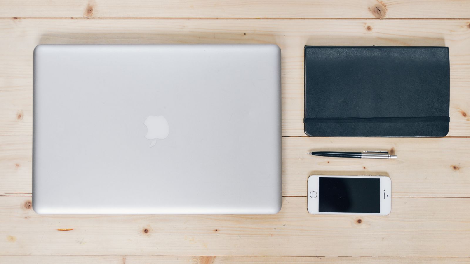 A clean, organized desk featuring a laptop, smartphone, notebook, and pen, ideal for productivity.