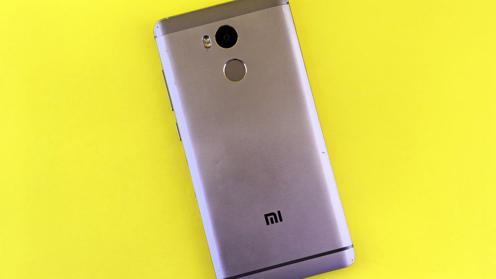 A silver smartphone placed on a bright yellow background, showcasing sleek design.