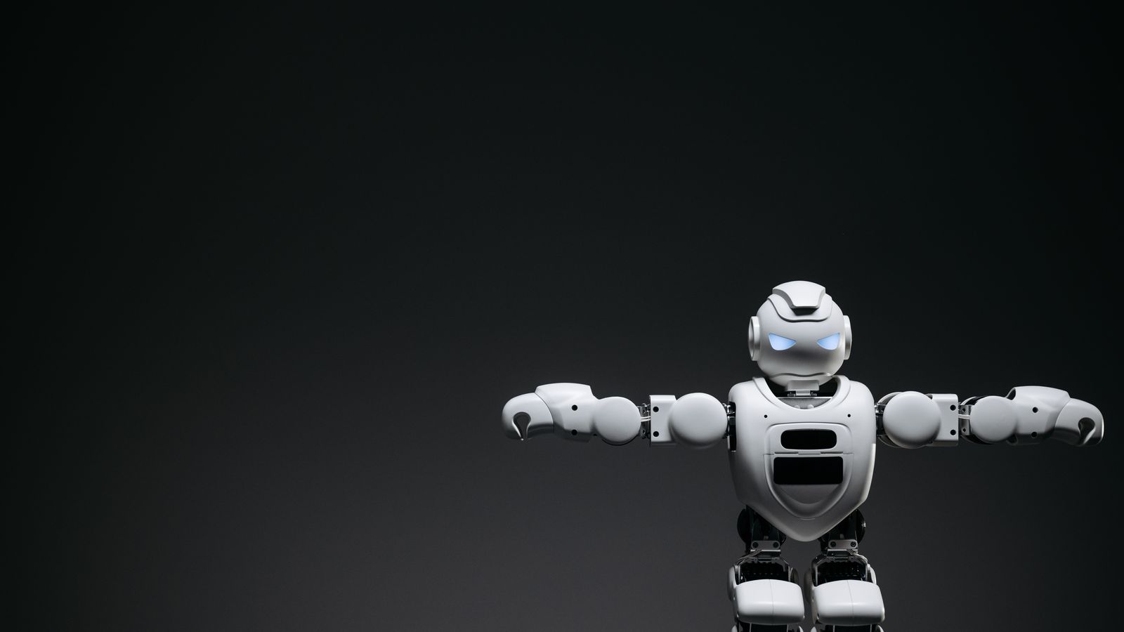 Studio shot of a humanoid robot with glowing eyes against a dark background, offering ample copyspace.