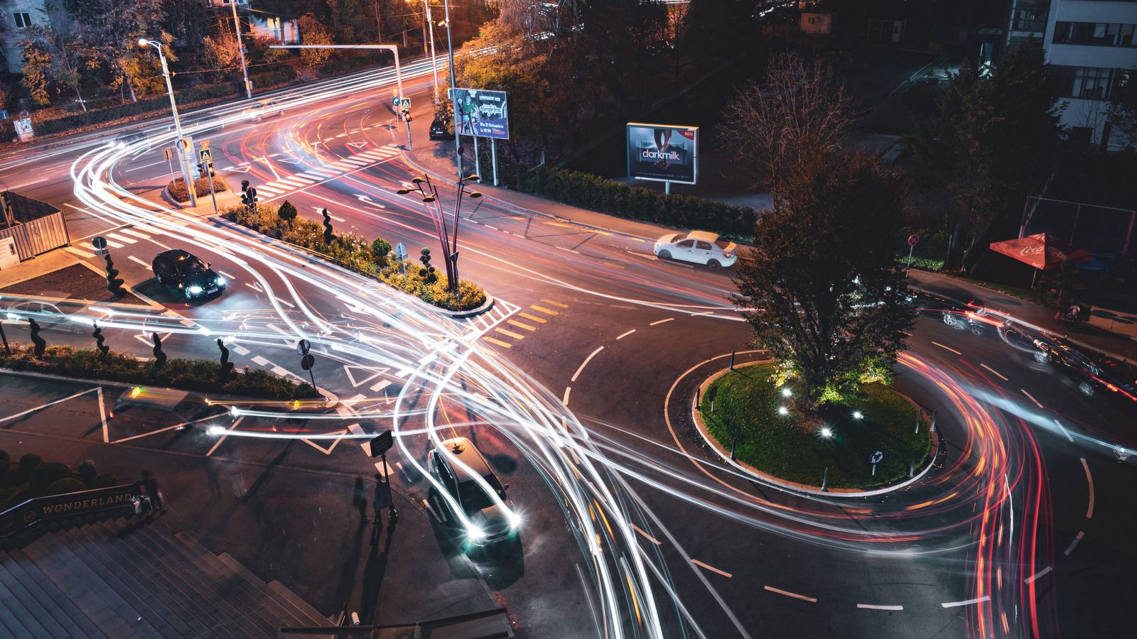 Aerial view of a bustling city intersection at night with vivid light trails from passing vehicles.