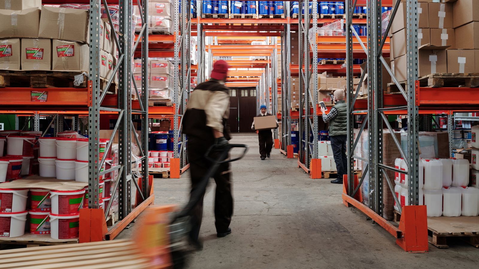 Warehouse interior with workers organizing shelves full of boxes and containers.