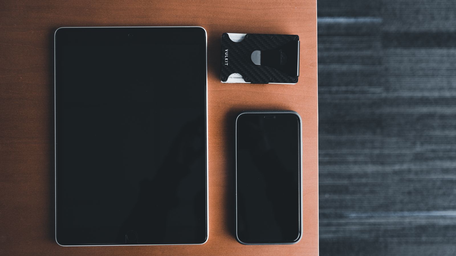 Top view of a tablet, smartphone, and card holder on a wooden surface, showcasing minimalist design.