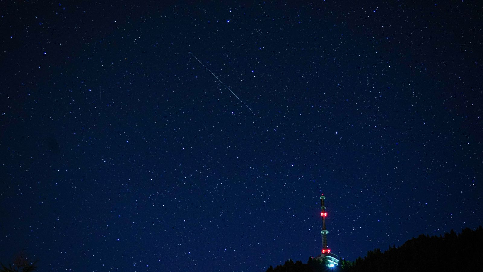 A mesmerizing view of a starry night sky with a broadcasting tower silhouette on the horizon.