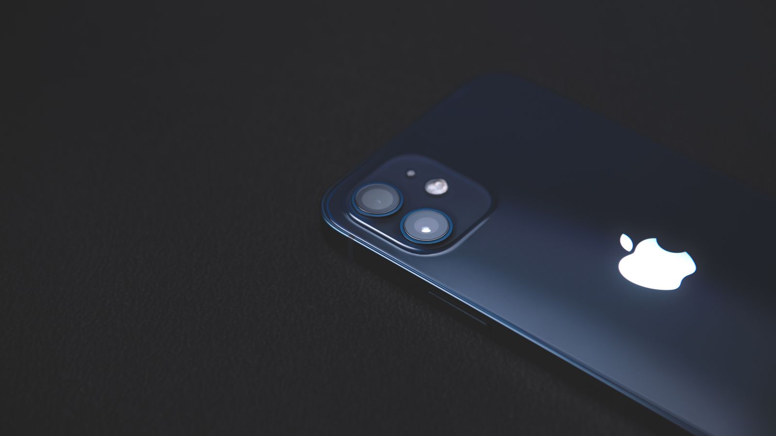 Close-up of a modern smartphone on a dark textured surface, highlighting its sleek design.