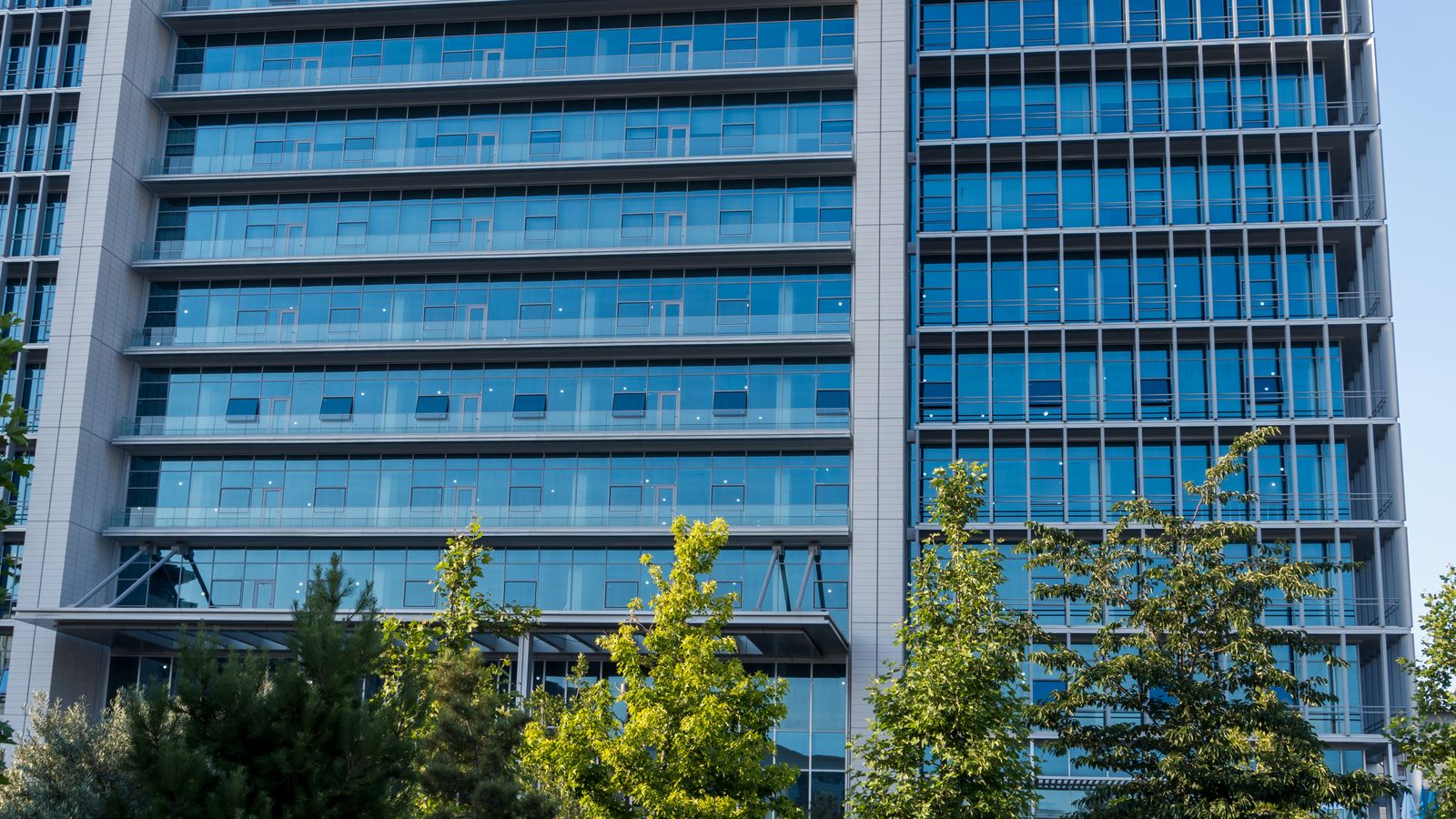 Glass facade skyscraper with trees in downtown urban scene, perfect for business and architecture themes.