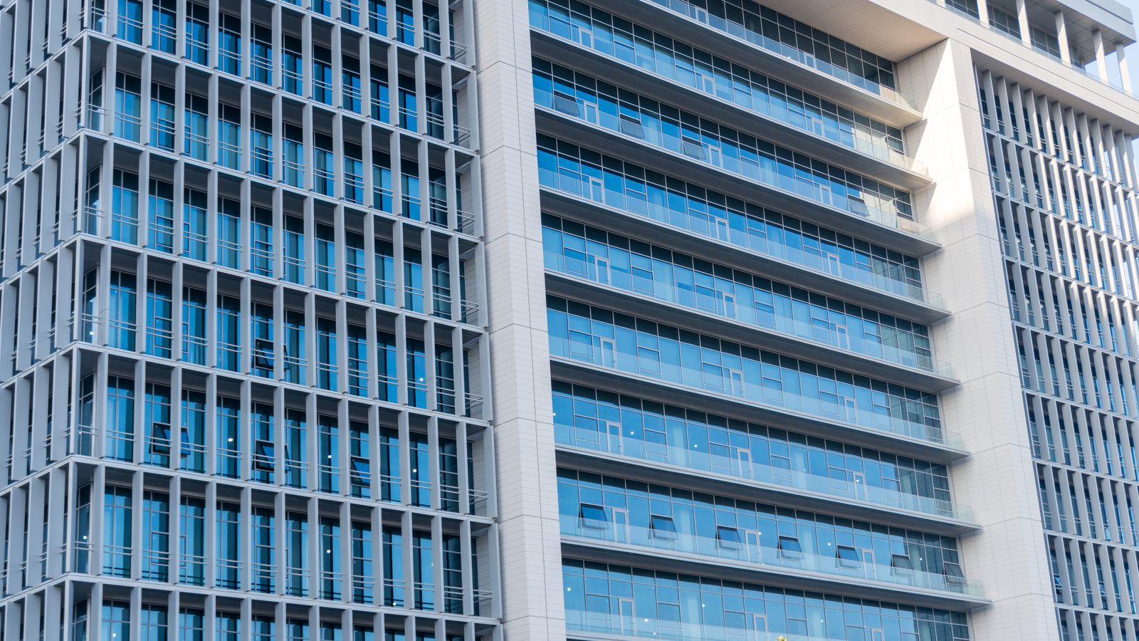 A modern office building with glass facade, featuring urban city architecture and blue sky reflections.