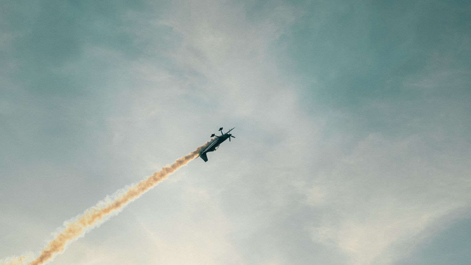 An aerobatic plane executes a vertical climb with a smoke trail in the clear sky.