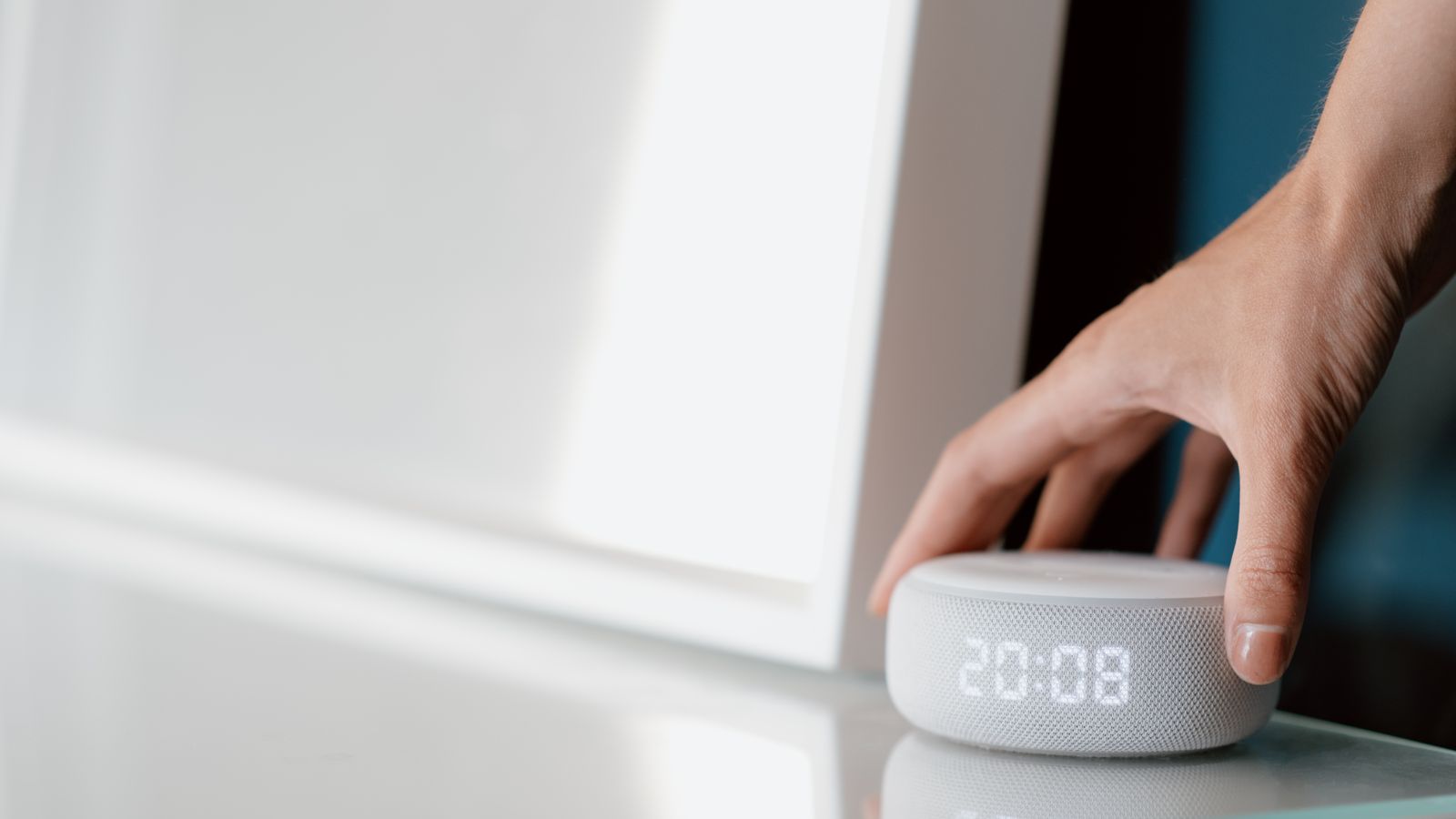Close-up of a hand adjusting a smart speaker displaying time indoors.