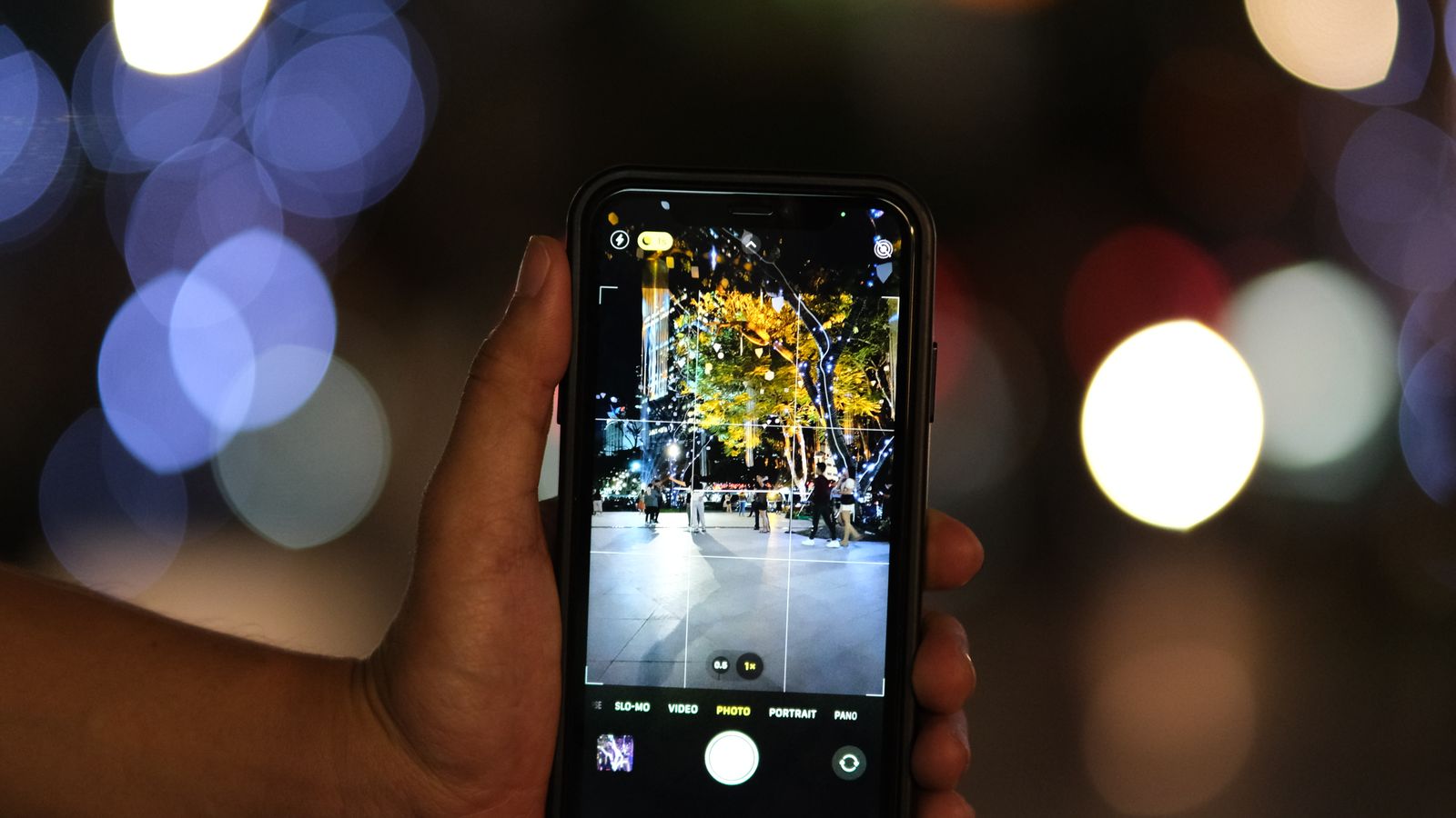 Vibrant image of a smartphone photographing a bustling night scene with bokeh effect.