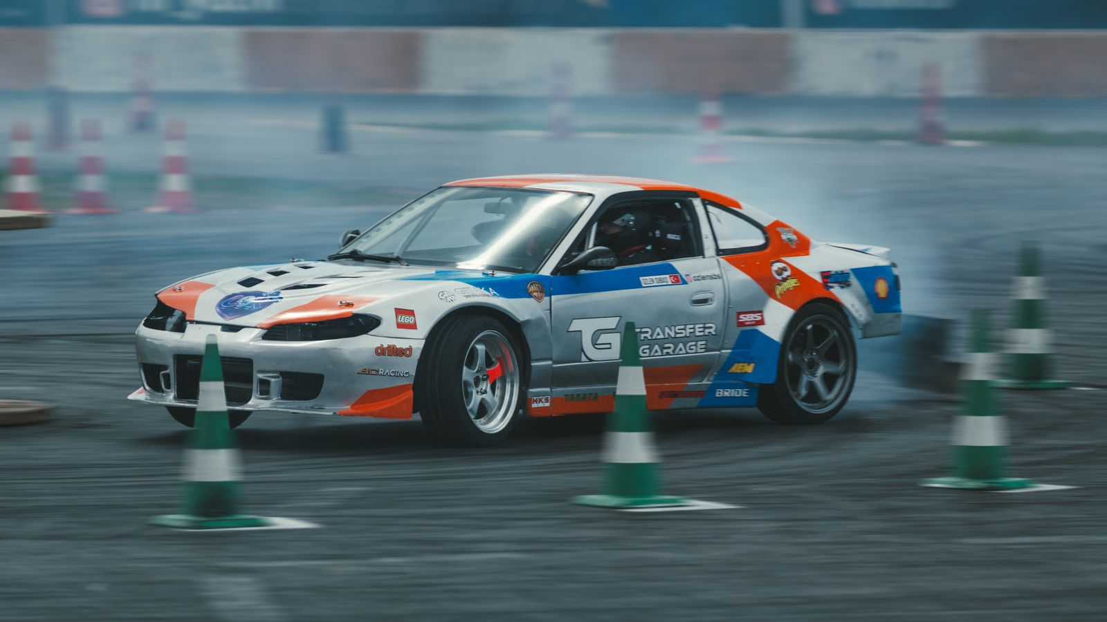 Action-packed scene of a customized car drifting around cones on a race track.