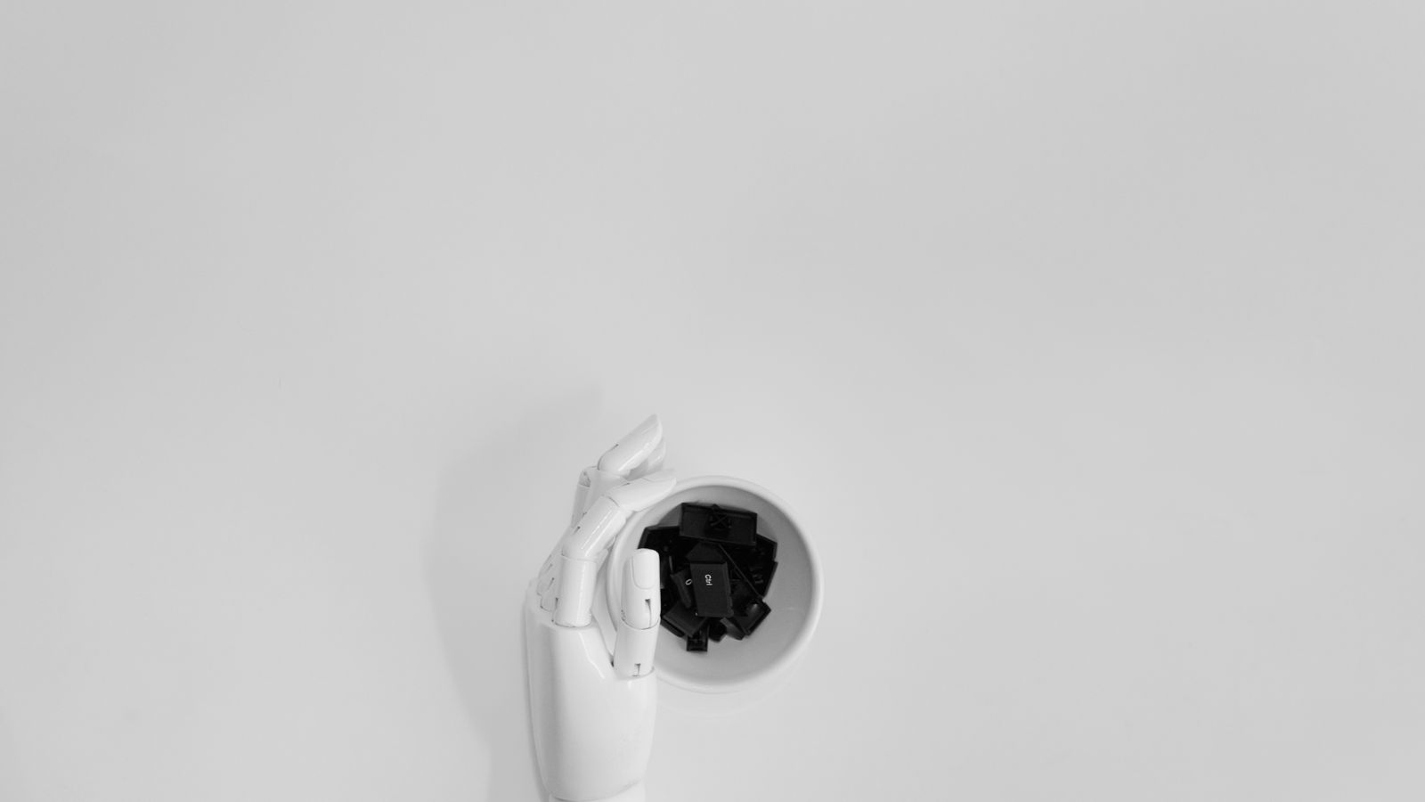 A robotic hand grasping black keyboard keys in a minimalist setting.