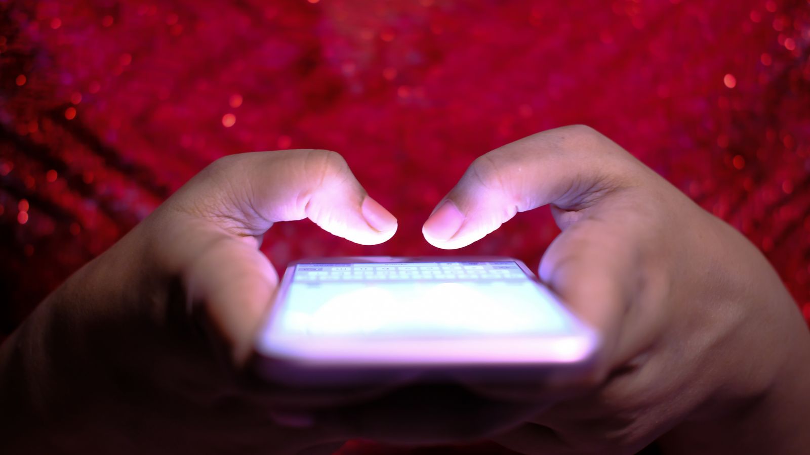 Hands typing on a smartphone with a glowing screen in low-light, highlighting technology and communication.