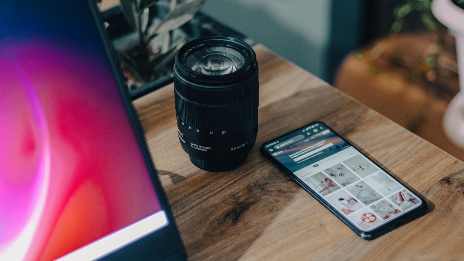 A camera lens beside a smartphone on a wooden desk, showcasing modern technology.