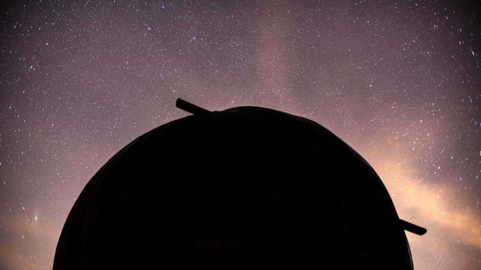 Silhouette of an observatory dome against a dramatic starry night sky.
