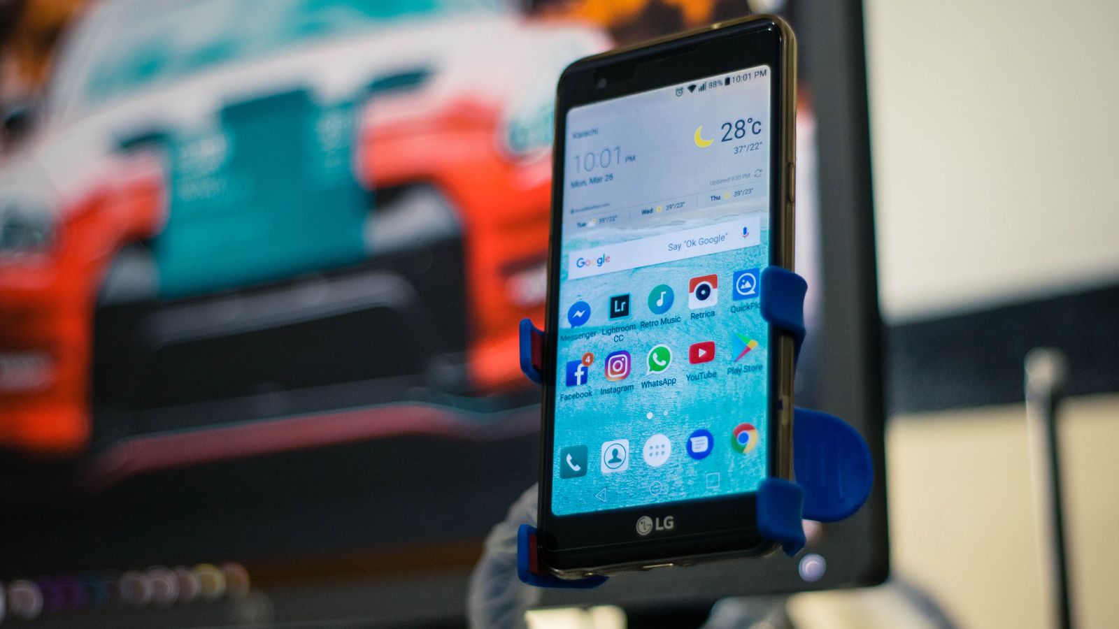 LG smartphone securely mounted in a car holder indoors, displaying various apps on the screen.