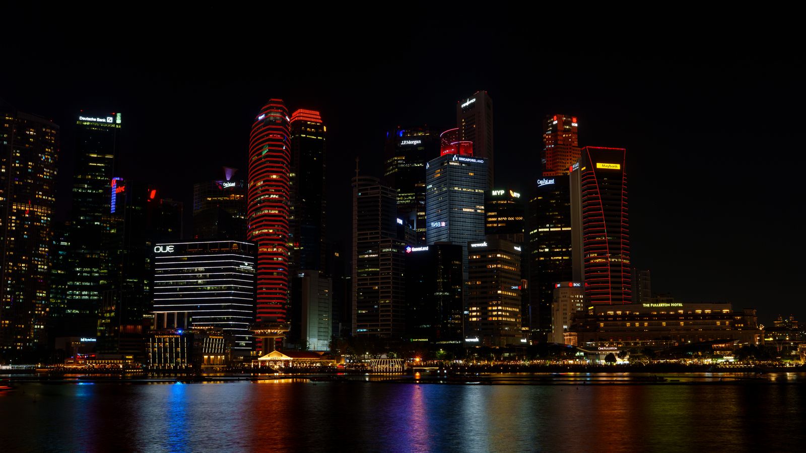 Vibrant nighttime cityscape of Singapore's illuminated skyline reflecting on water.