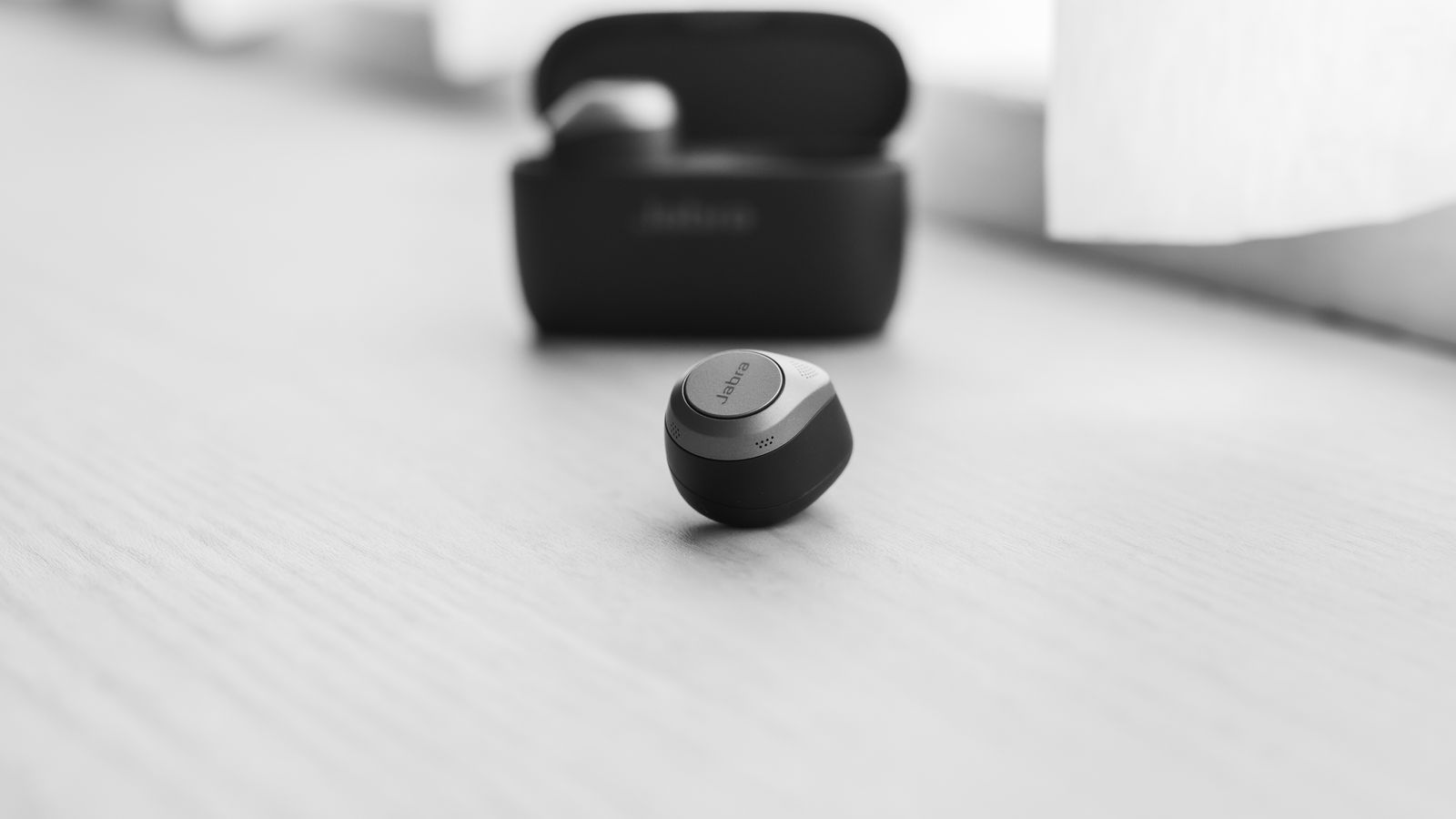 Monochrome close-up of a single wireless earbud on a wooden surface.