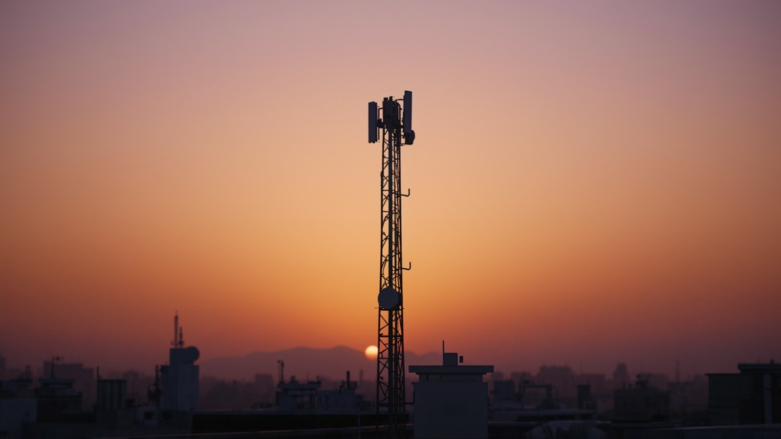 Cellular antenna mast silhouetted over a city at sunset