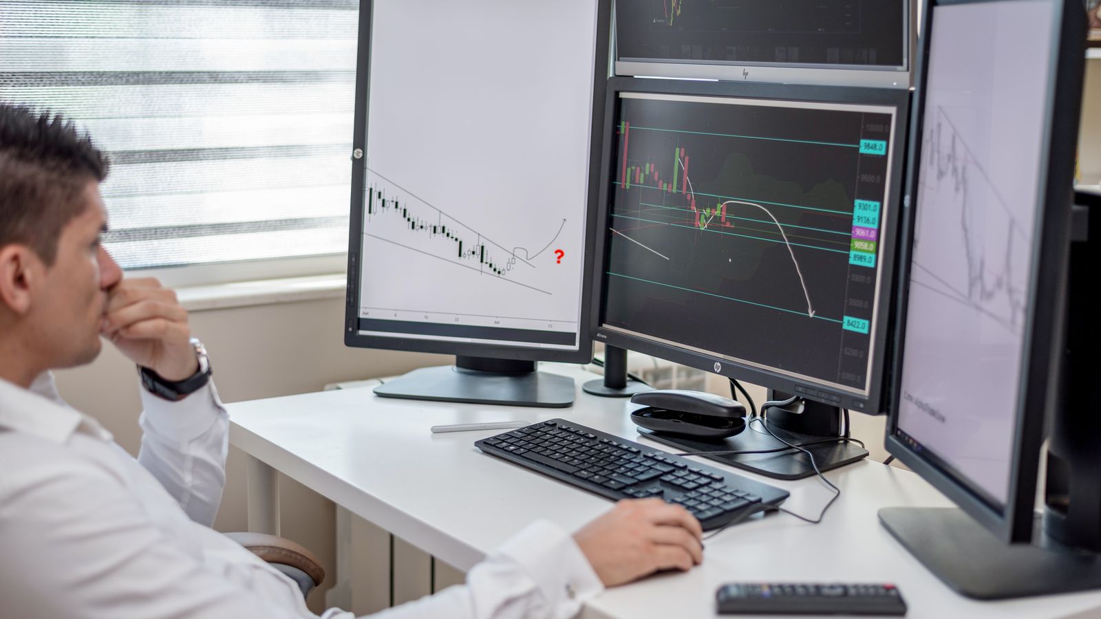 Business professional analyzing financial data on multiple computer monitors at his workspace.