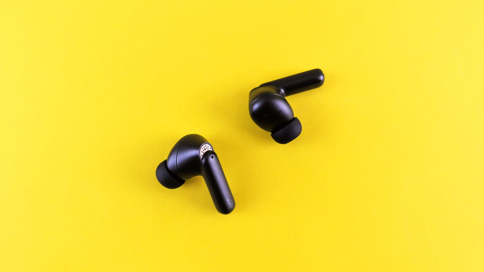 Minimalist black wireless earbuds on a bright yellow backdrop for tech and lifestyle themes.