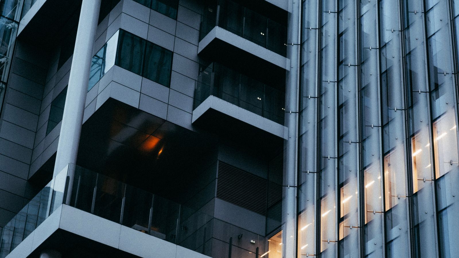 Low angle view of modern office building with glass facade and ambient lighting at dusk.