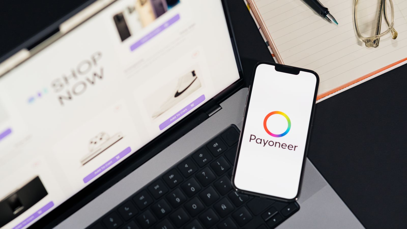 Mobile phone with Payoneer app on screen next to laptop displaying online shopping site.