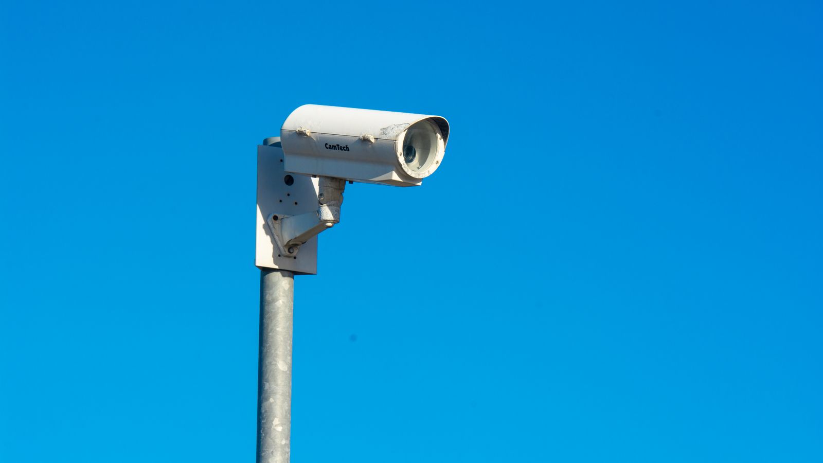 White security camera mounted on a pole under a clear blue sky, symbolizing security and surveillance.