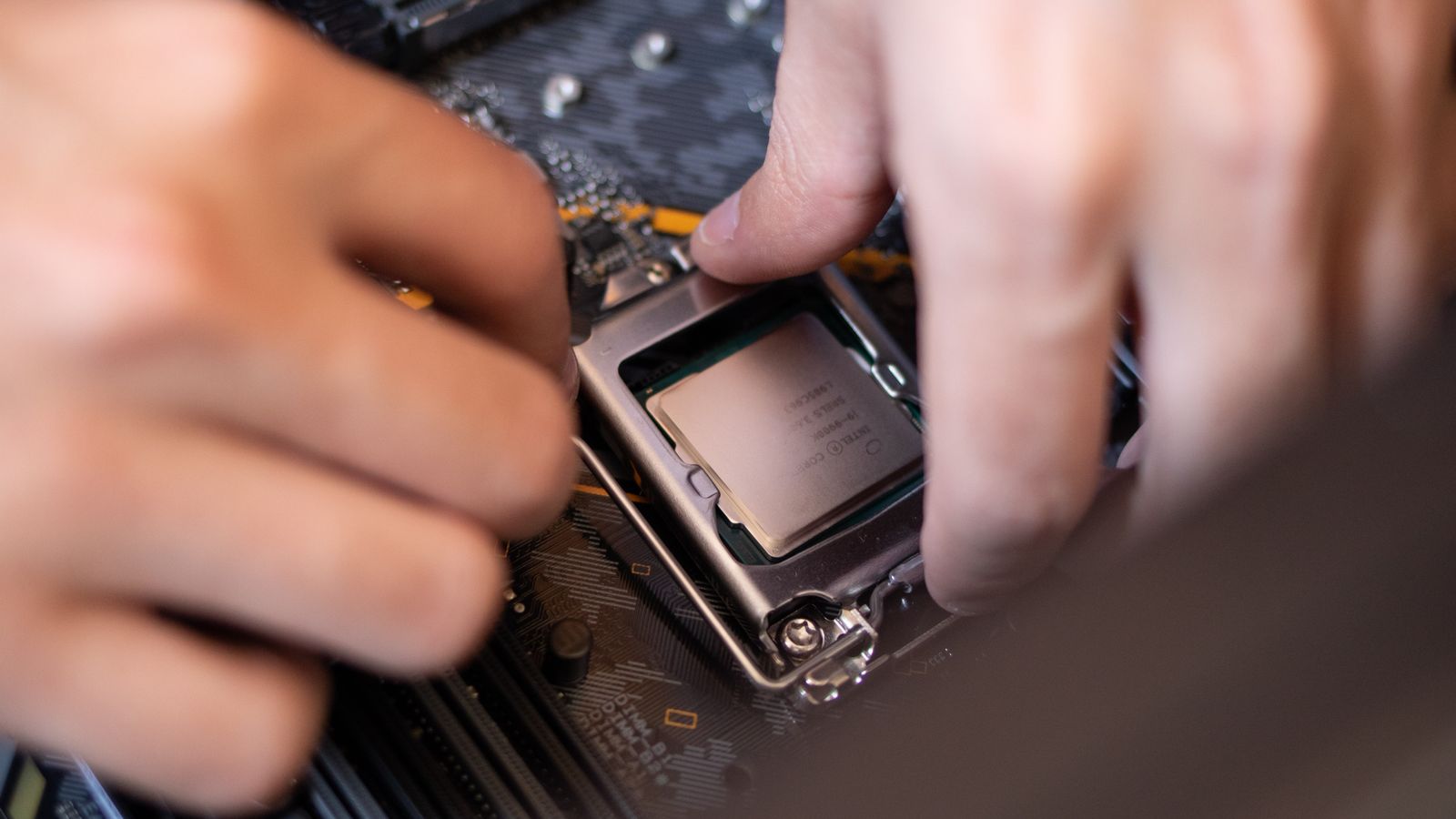 Detailed view of hands installing a CPU onto a motherboard inside a computer setup.