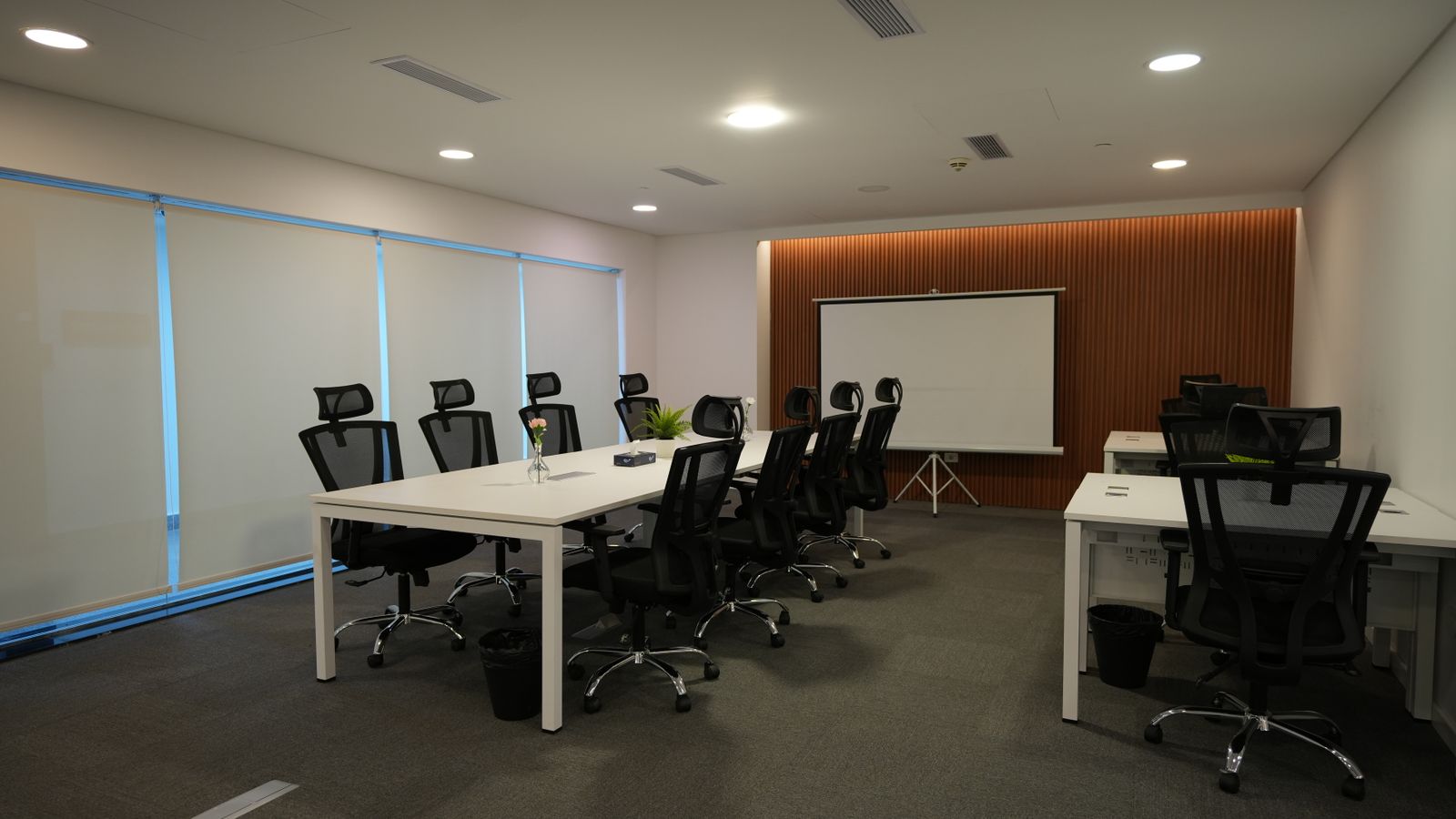 Spacious and well-lit conference room featuring ergonomic chairs, large tables, and a projector screen.