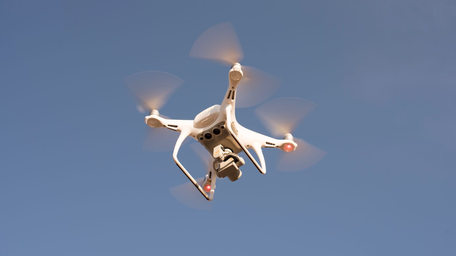 A white drone in flight against a clear blue sky, capturing aerial footage with precision.