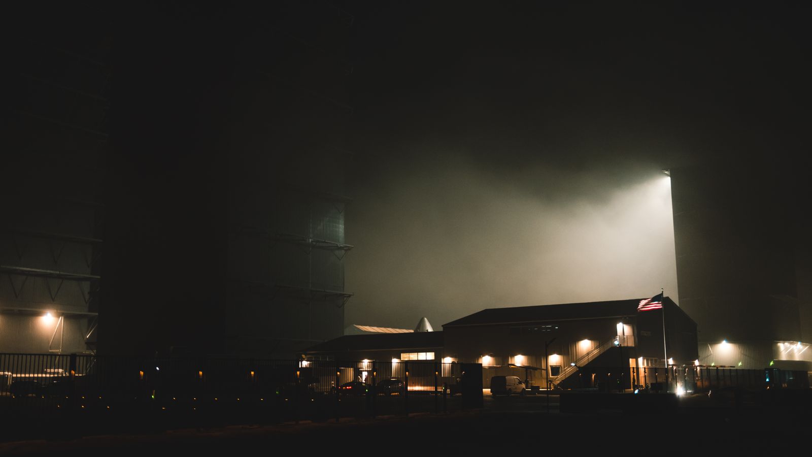 A dramatic nighttime view of an industrial facility at a space exploration center with atmospheric lighting.
