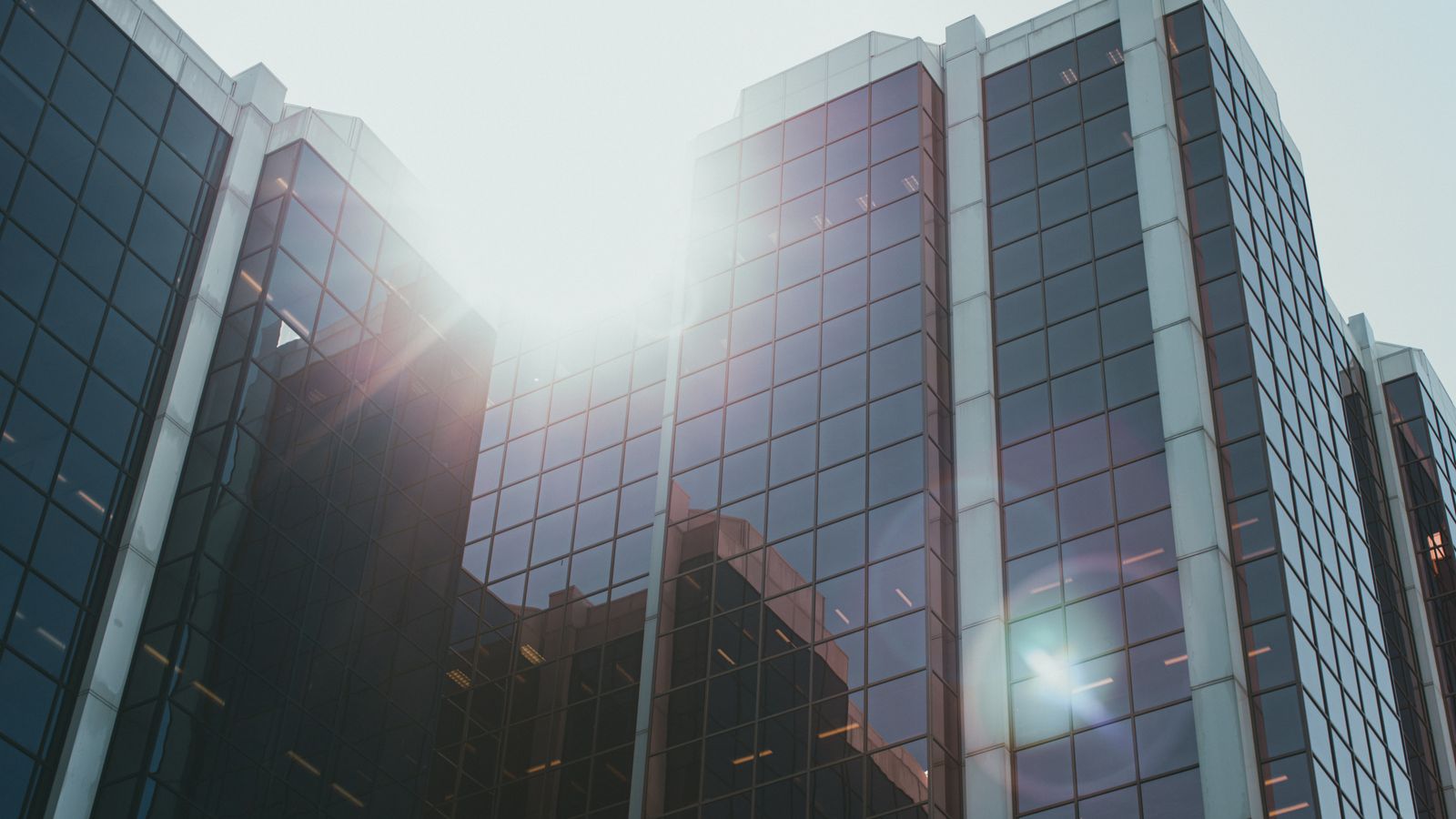 Low angle view of a modern glass skyscraper with sunlight reflecting off the facade.