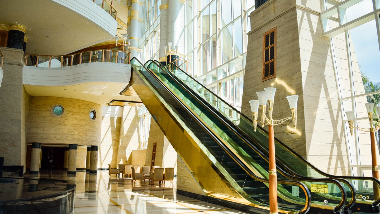 A modern glass escalator in a spacious atrium with bright natural lighting.