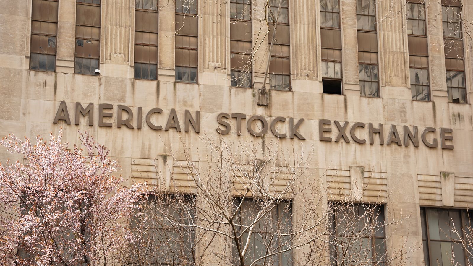 Facade of the American Stock Exchange Building in New York City during spring with blooming trees.