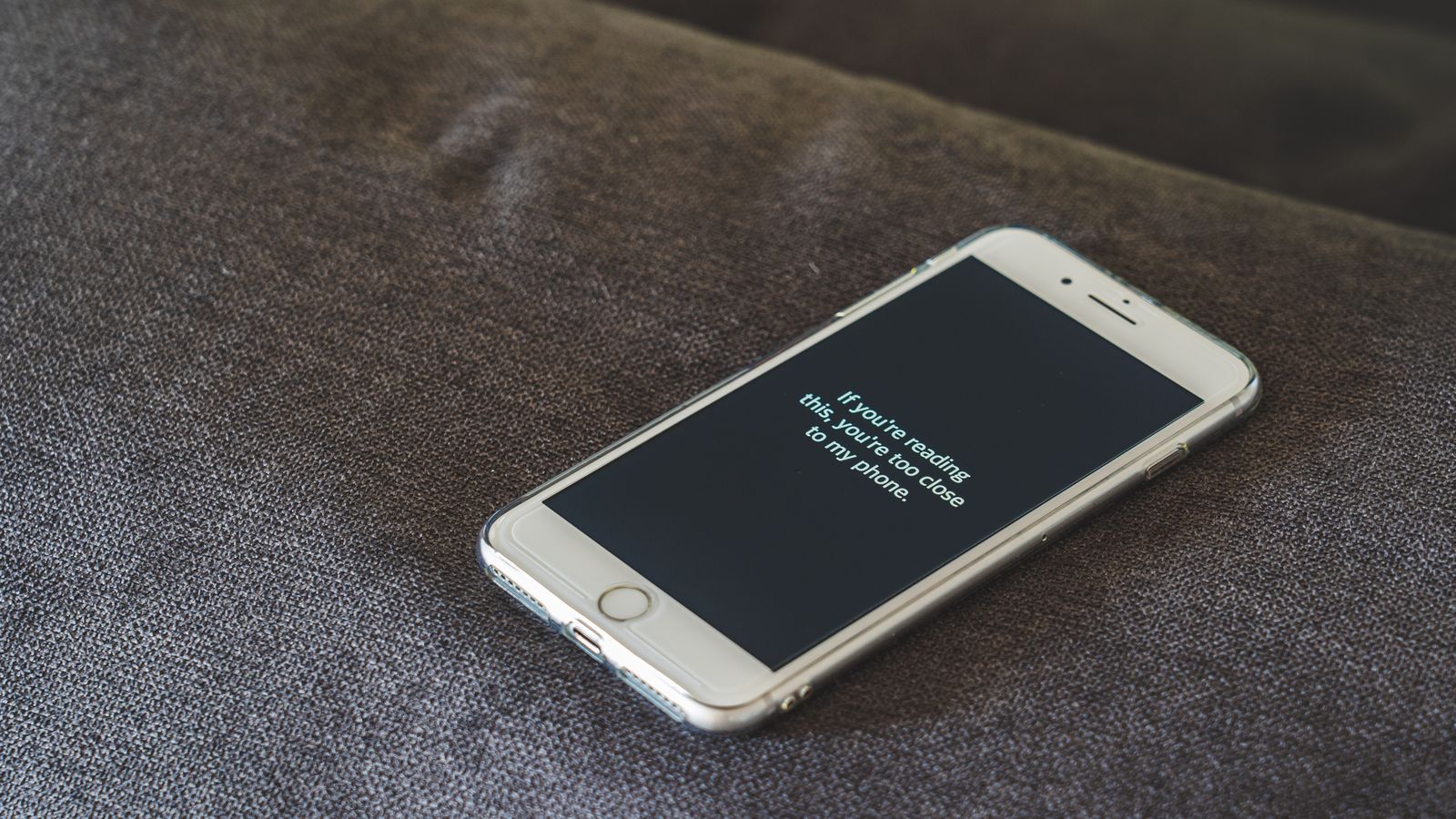 A smartphone with a humorous lock screen message placed on a grey couch, emphasizing privacy.