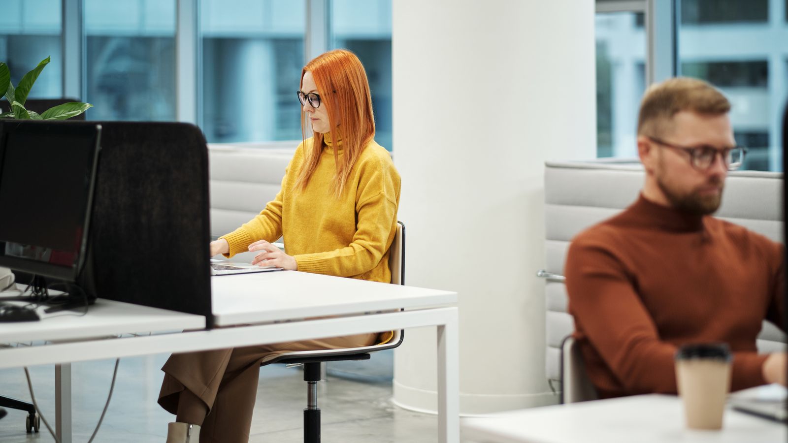 Two professionals working in a contemporary office environment with computers and casual attire.