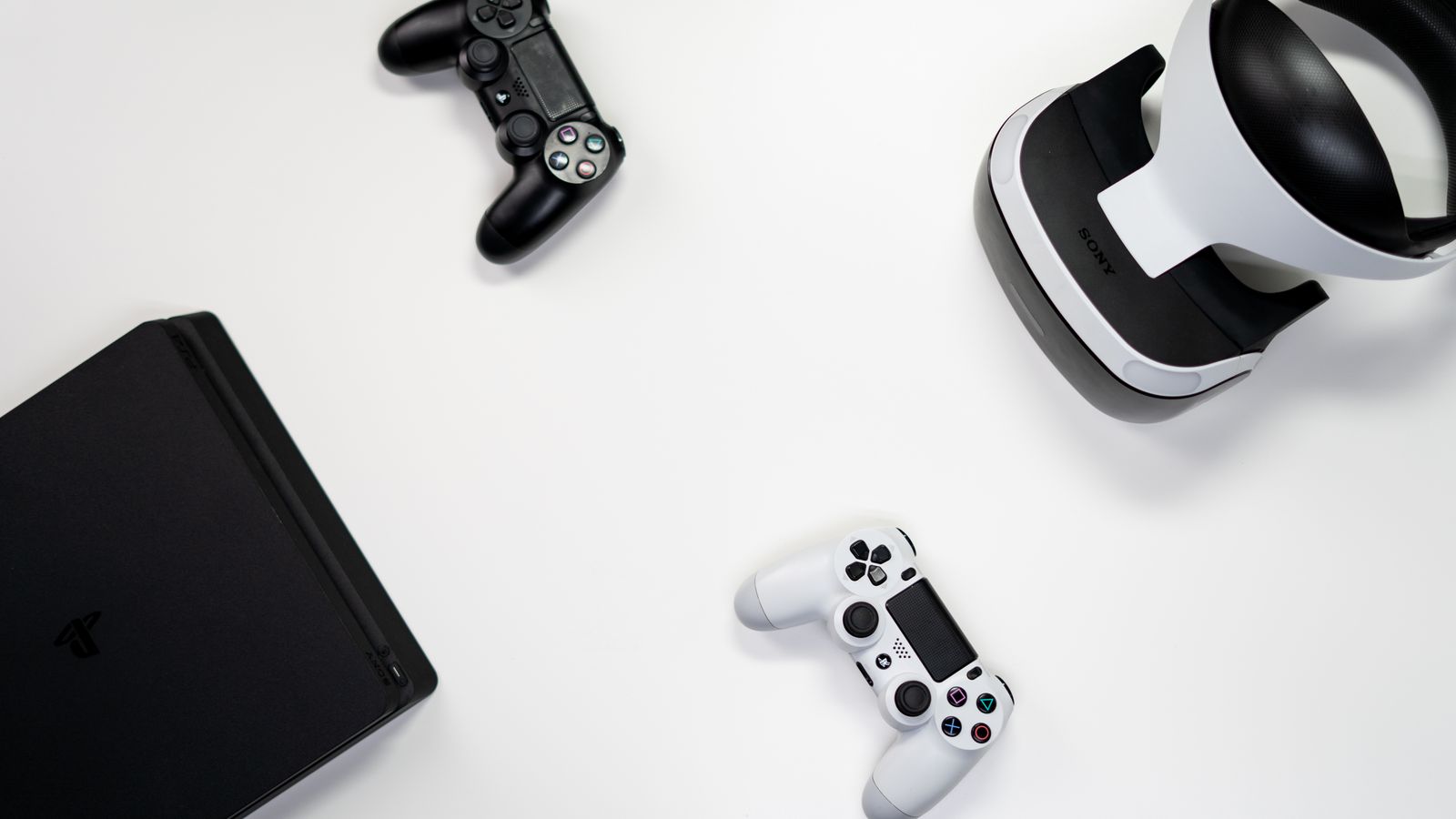 Flat lay of gaming console, controllers, and VR headset on a white background.