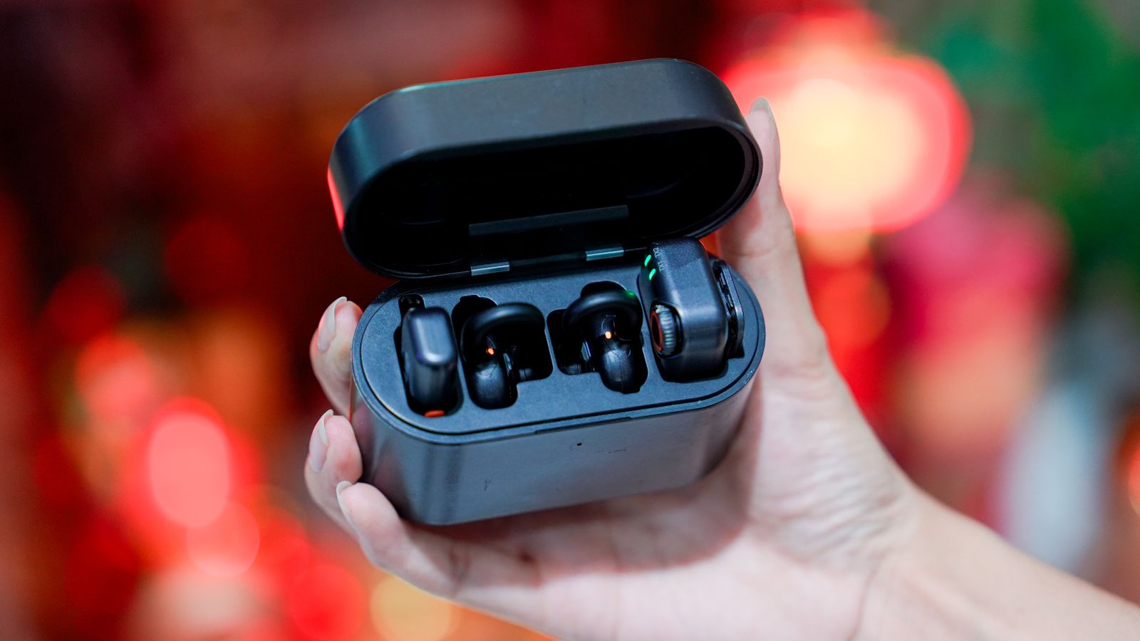 A hand holds a pair of black wireless earbuds in an open charging case.