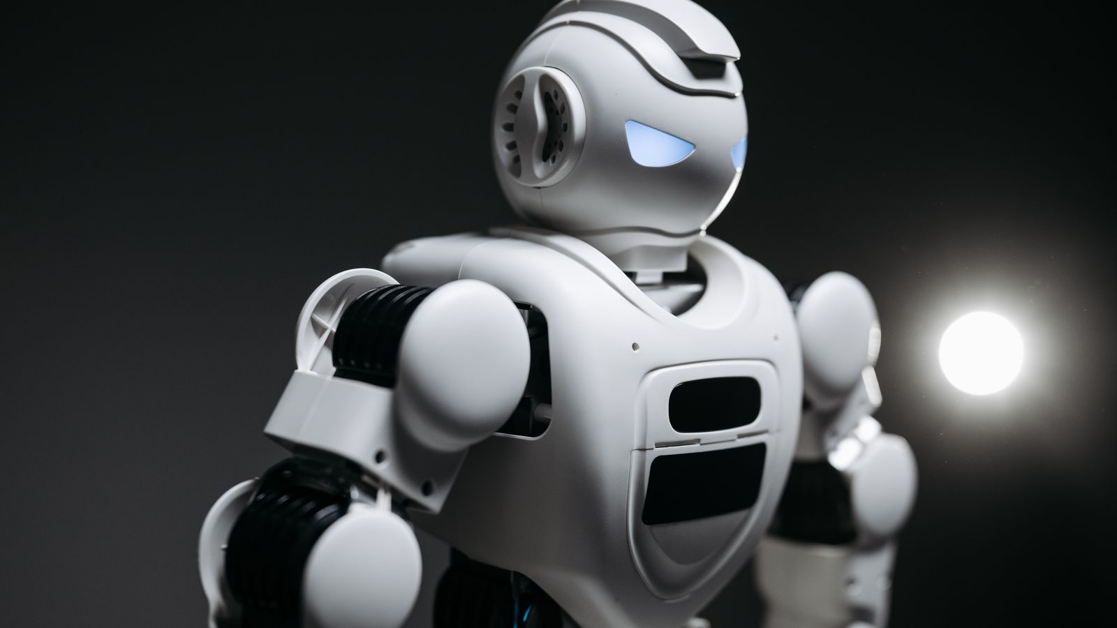 High-detail close-up image of a white robot with glowing eyes in studio lighting. Modern tech innovation.