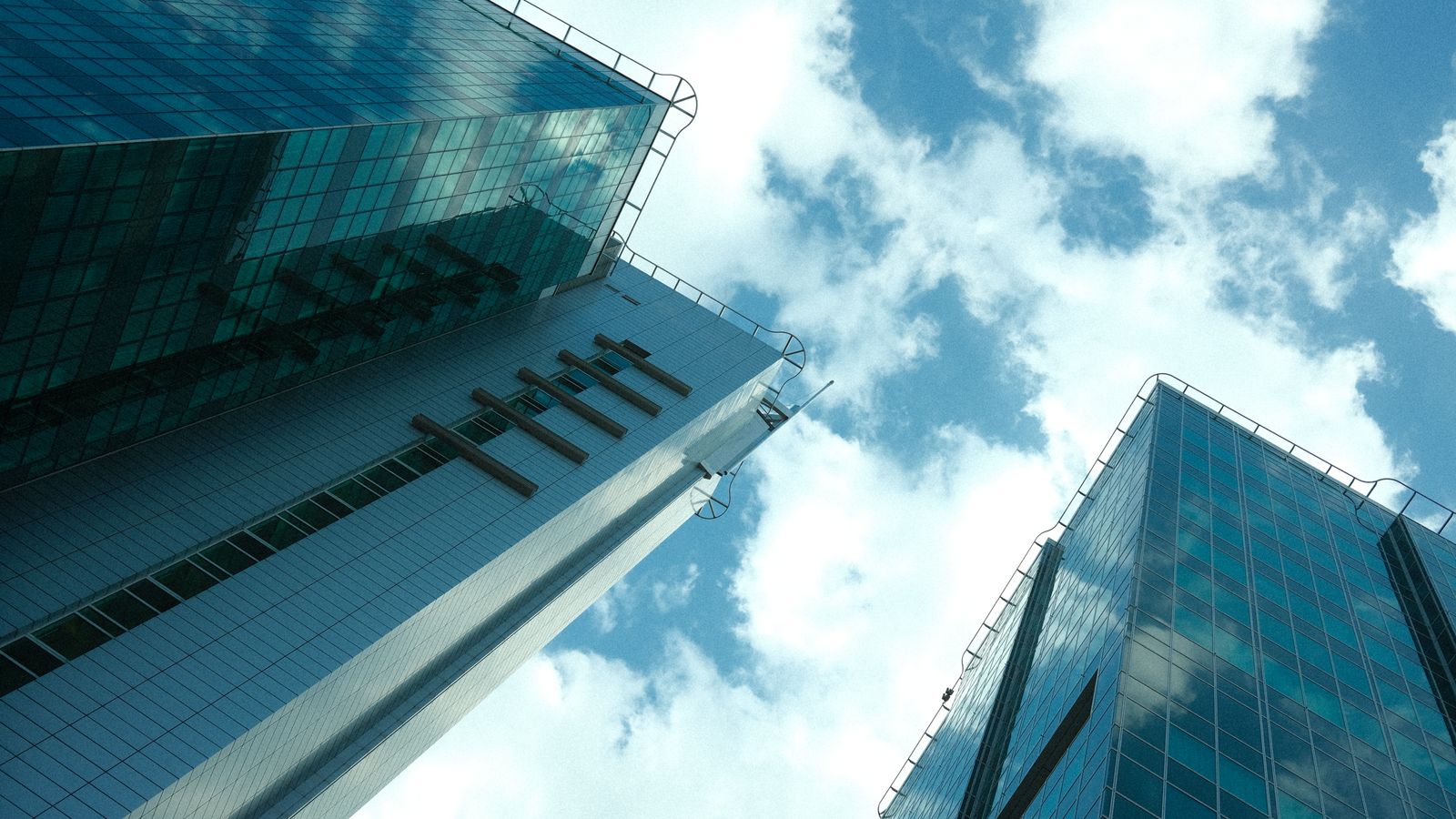 Low angle view of modern glass skyscrapers with clouds reflecting, under a bright blue sky.