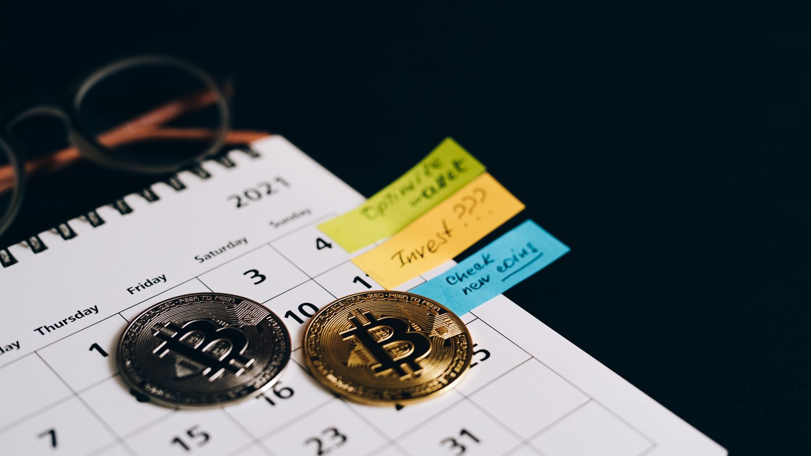 Bitcoin coins placed on a calendar with sticky notes for investment planning.