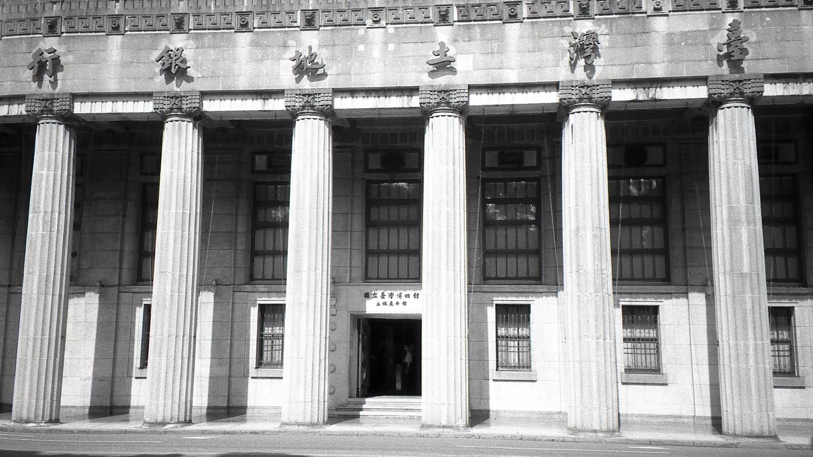 Exterior of historic national bank with decorative elements on classic columns located in city with modern building against blue sky