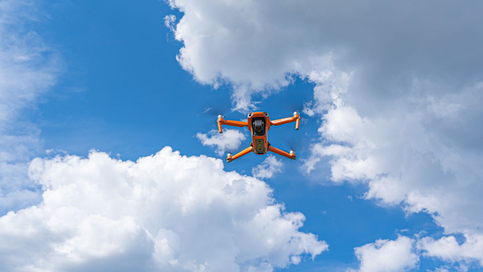Orange drone flying against a dramatic cloudy sky, showcasing modern technology and aerial expertise.