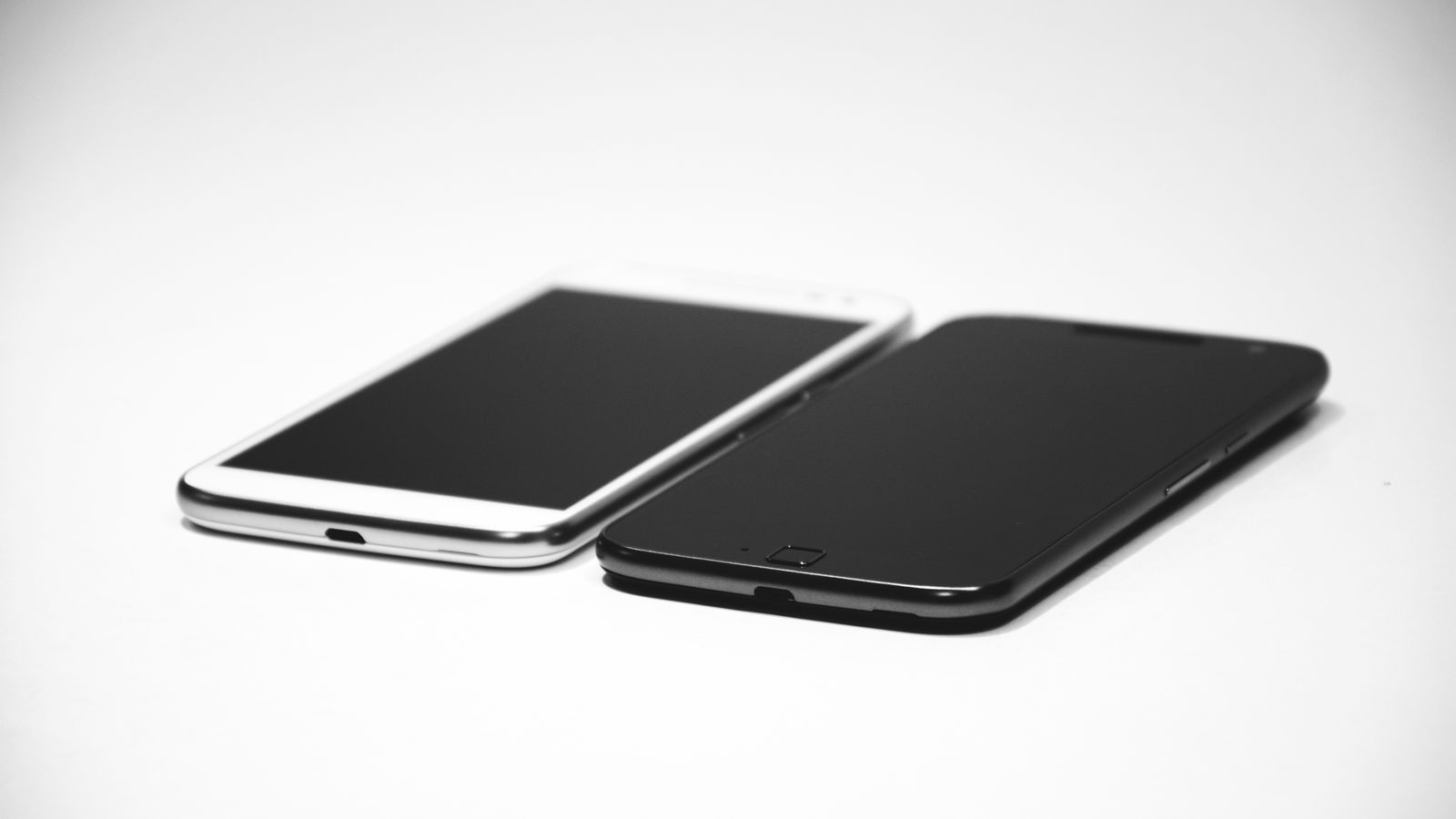 Two smartphones, one black and one white, placed on a white surface, showcasing modern design.