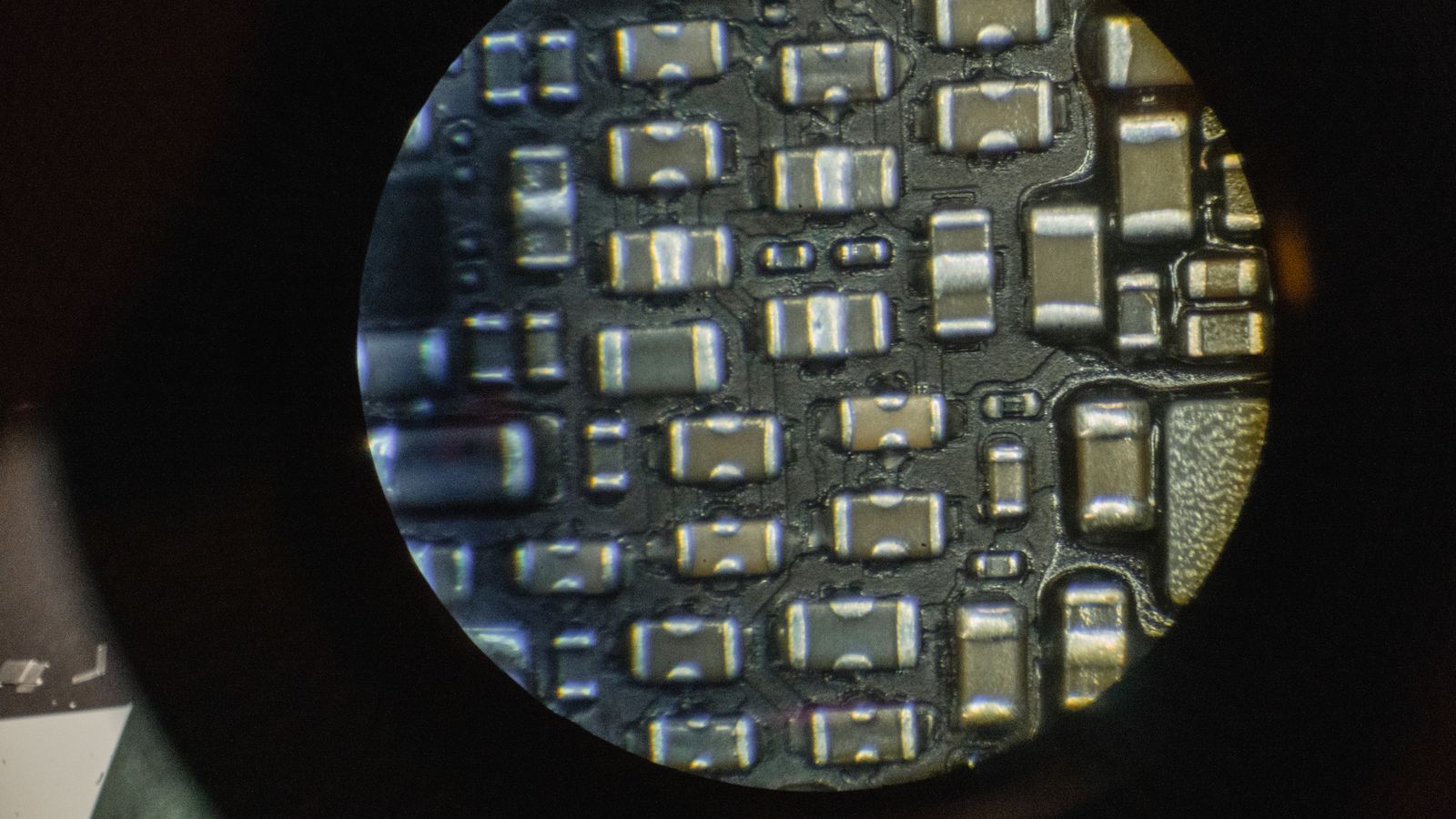 Large dark chip package with rows of gold contacts along its edges, lying on a matte dark surface