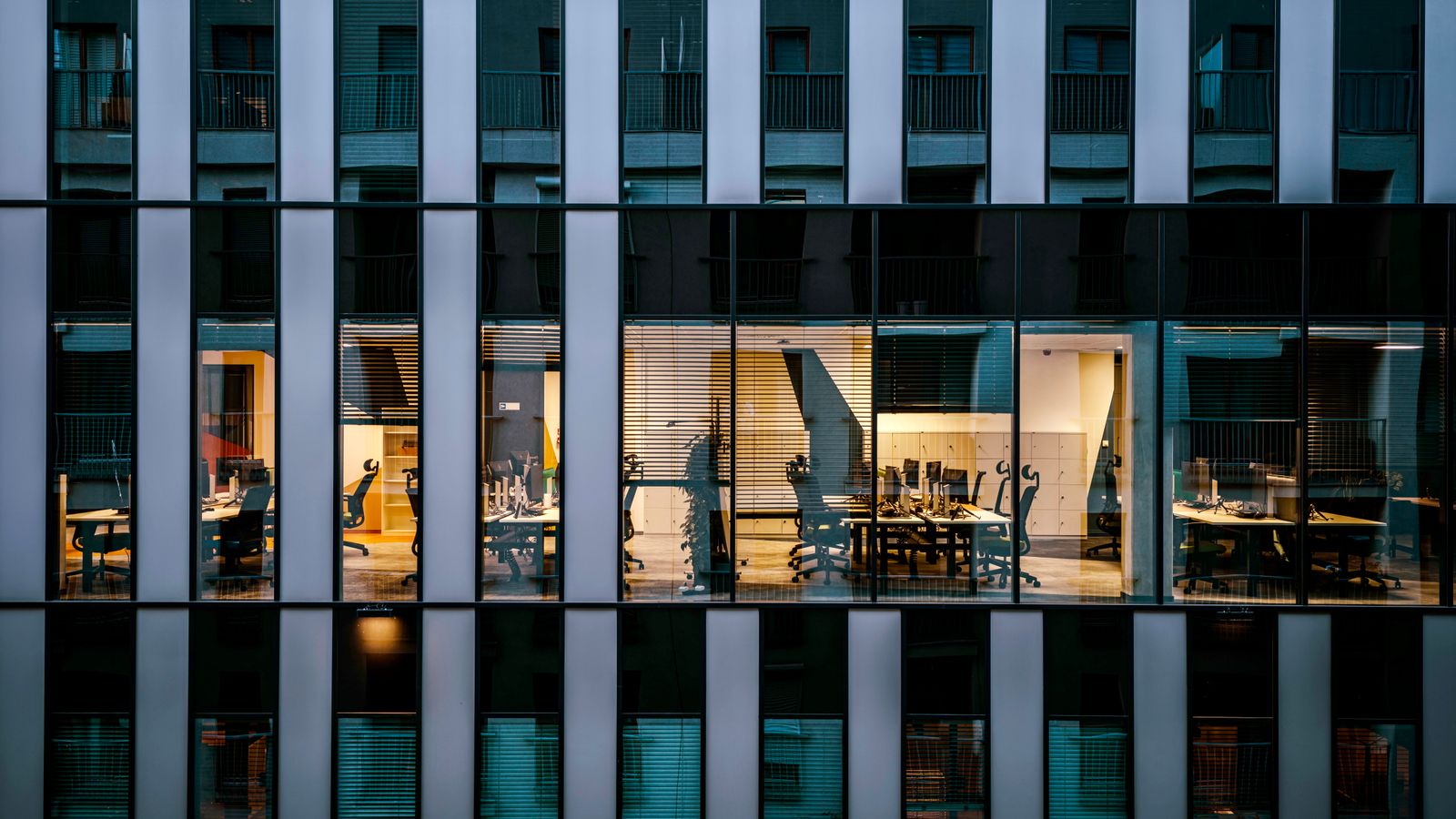 Illuminated office inside a modern glass building exterior, showcasing architecture and workspace design.