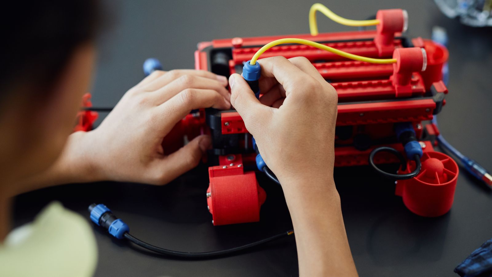 Close-up of hands assembling a robotic project with cables indoors, showcasing technology and electronics.