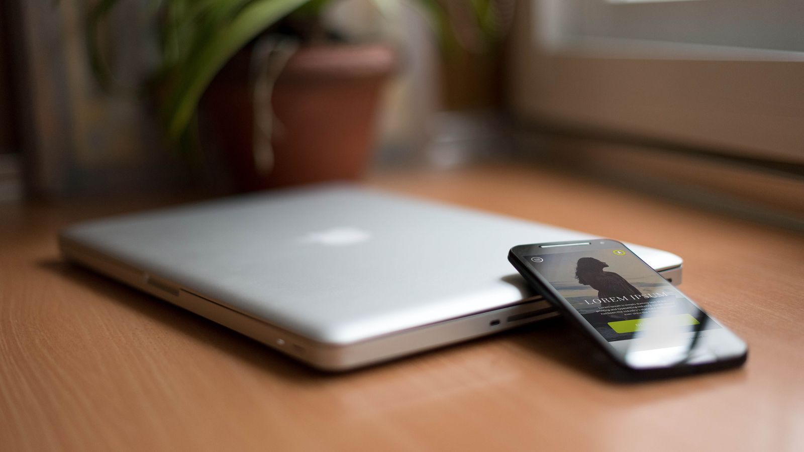 Close-up of a silver laptop and smartphone on a wooden desk, capturing modern work essentials.
